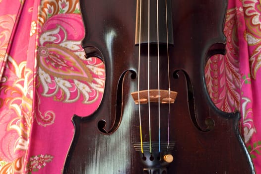 Old violin against bright pink paisley background.Violin is an antique from the early 1800's in a dark stain (original finish).