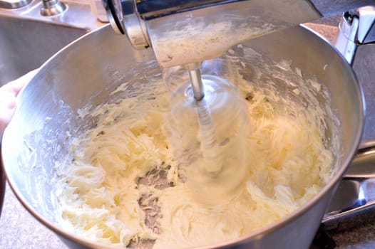 Stainless steel stand mixer at high speeding whipping homemade icing ingredients together.