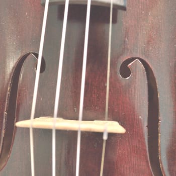 Closeup of a violin bridge and f holes, faded for text overlay.Violin is an antique from the early 1800's in a dark stain (original finish). Square composition.