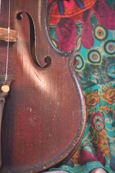 Closeup of a violin against a bright, artsy fabric background. Violin is an antique from the early 1800's in a dark stain (original finish). Vertical orientation.