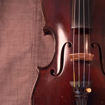Old violin against gray seamed fabric. Violin is an antique from the early 1800's in a dark stain (original finish). Square image with copy space.