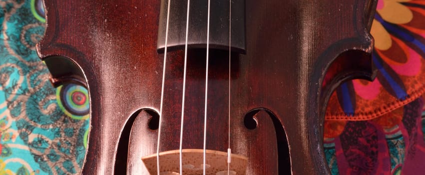 Extreme widescreen view of  the middle part of a violin.Closeup of a violin against a bright, artsy fabric background. Violin is an antique from the early 1800's in a dark stain (original finish).