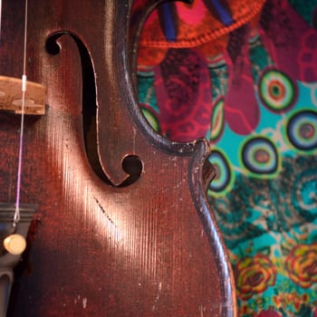 Closeup of old violin against a colorful print. Violin is an antique from the early 1800's in a dark stain (original finish). Square composition.