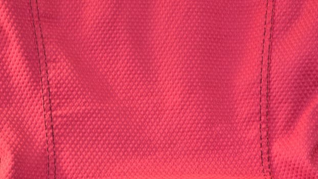 Vivid hot pink fabric background. Closeup of a textured pink fabric with black stitch detailing on both sides. Letterbox shape.