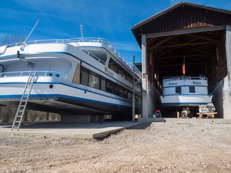 Rear view of the motor ship MS Füssen in the drained Foggen Lake at the boathouse for inspection in sunny spring weather and blue skies.