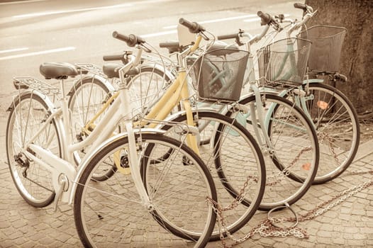 Four parked bicycles on the sidewalk, chained together.  Vintage effect.