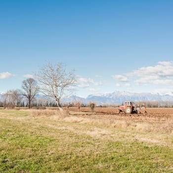 Agricultural landscape. With tractor plowing a field. The mountains in the background.