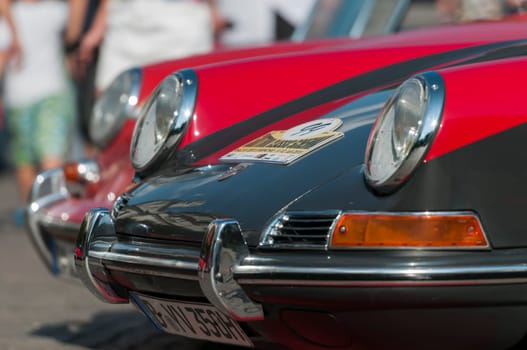 side view of the bumpers and headlights of several consecutive poches 911 on the Passer promenade in front of the Kur-Haus during the South Tyrol Classic Cars Rallye 2015. Interested spectators in the fuzzy HIntergrund