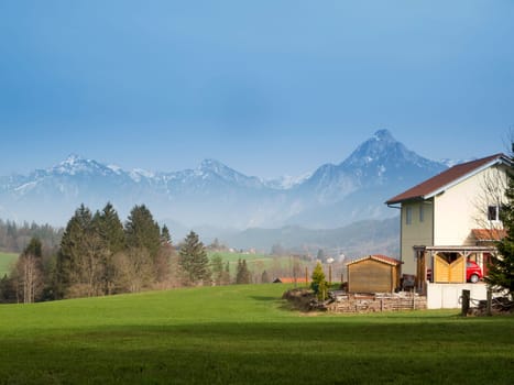 Allgäu landscape with house in the foreground,meadow and forest in the middle of the picture and alpine mountains in the background
