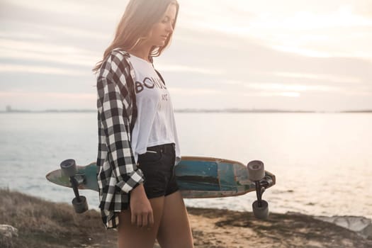 Beautiful and fashion young woman posing at the sunset with a skateboard
