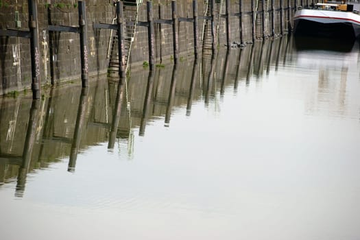 The pillars of a ship pier are reflected in the water of a dock.