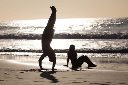 Silhouette of happy couple having fun on beach, man doing headstand.