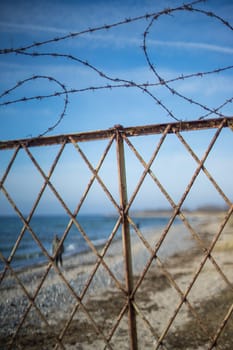 old stab wire fence on the beach in front of blue water