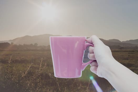 Woman hand holding coffee cup with sunrise, stock photo