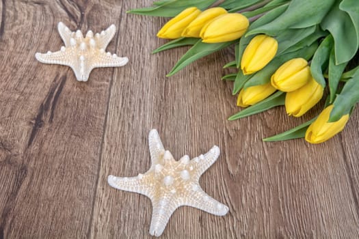 Starfishes and yellow tulips on a wooden background