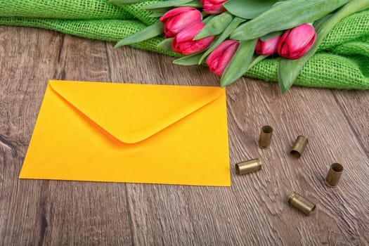 Yellow envelope, tulips and bullets on a wooden background