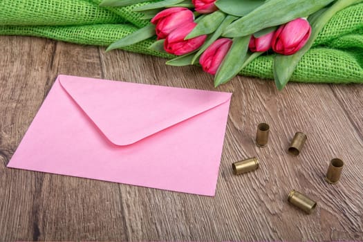 Pink envelope, tulips and bullets on a wooden background