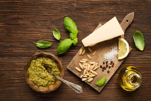 Fresh basil pesto with ingredients on wooden background.