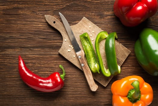 Red, green and orange bell peppers on wooden background.