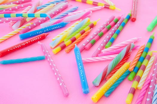 Various colorful birthday candles scattered on pink