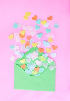 Colorful heart confetti from green envelope on pink
