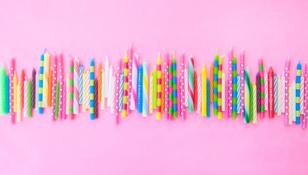 Various colorful birthday candles lined up on pink