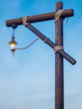 luminous lantern on a gallows-shaped wooden construction held together by ropes in front of blue sky in the early twilight in Neuharlingersiel / Friesland