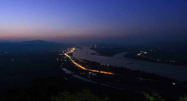 Aerial landscape view of Mekong river with mountain ranges at twilight in Nong Khai Province, Thailand. Long exposure shot with street light trails