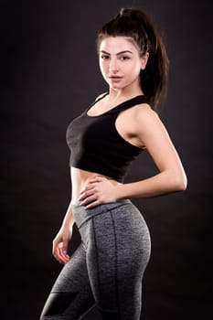 pretty brunette wearing fitness outfit on dark black background