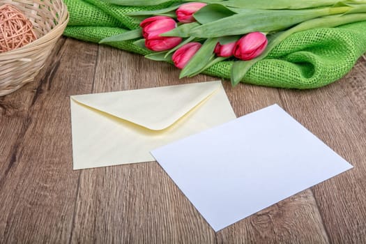 Envelope with sheet of paper and red tulips on a wooden background
