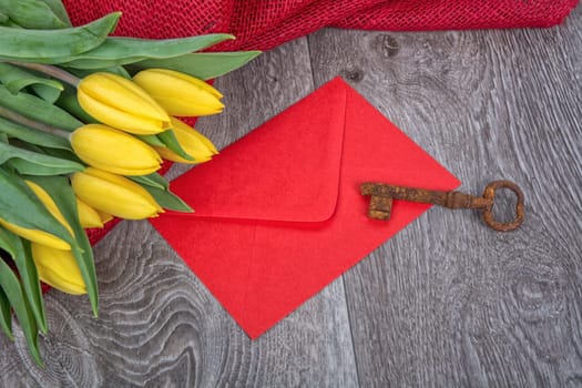 Envelope, rusty key and yellow tulip on a wooden background