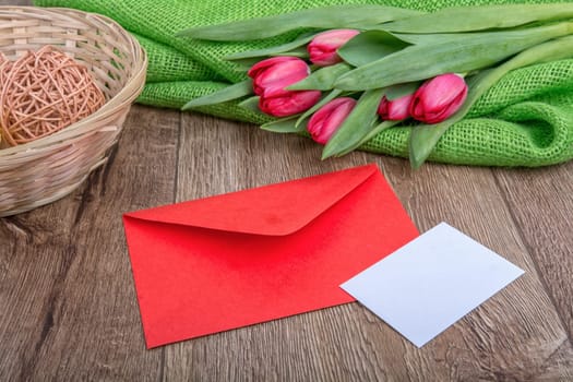 Envelope with sheet of paper and red tulips on a wooden background