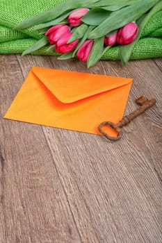 Envelope, rusty key and red tulip on a wooden background