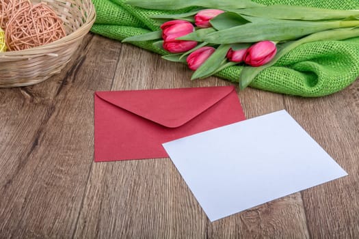 Envelope with sheet of paper and red tulips on a wooden background