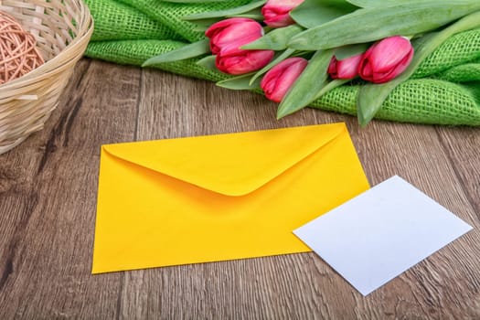Envelope with sheet of paper and red tulips on a wooden background