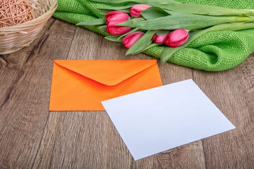 Envelope with sheet of paper and red tulips on a wooden background