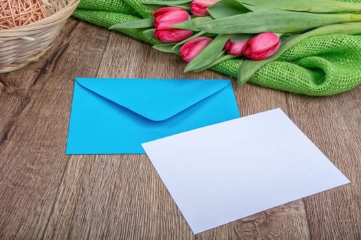 Envelope with sheet of paper and red tulips on a wooden background