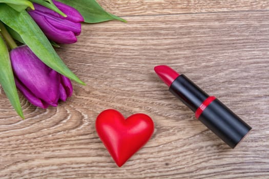 Lipstick, red heart and purple tulips on a wooden background