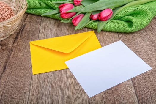 Envelope with sheet of paper and red tulips on a wooden background