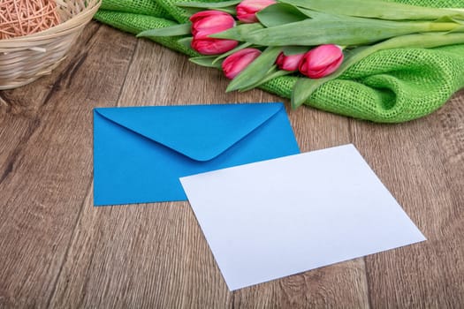 Envelope with sheet of paper and red tulips on a wooden background