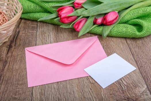 Envelope with sheet of paper and red tulips on a wooden background