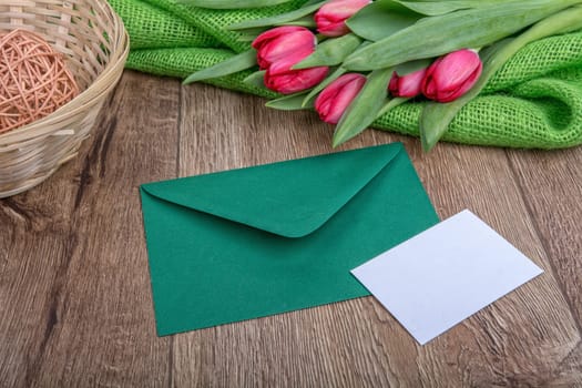 Envelope with sheet of paper and red tulips on a wooden background