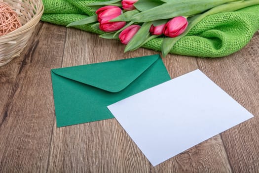 Envelope with sheet of paper and red tulips on a wooden background