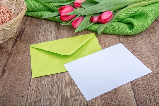 Envelope with sheet of paper and red tulips on a wooden background