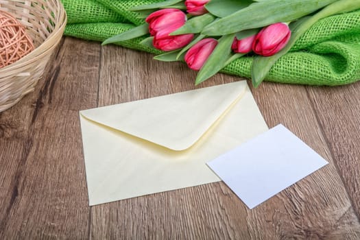 Envelope with sheet of paper and red tulips on a wooden background