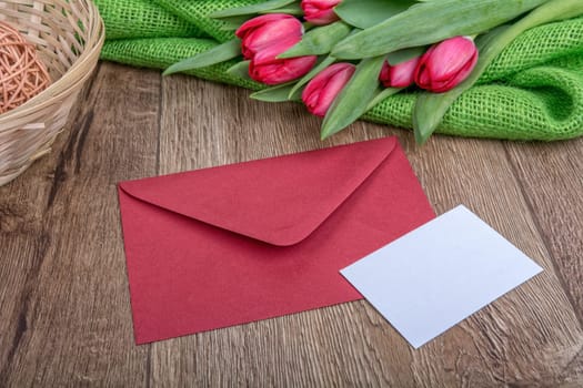 Envelope with sheet of paper and red tulips on a wooden background