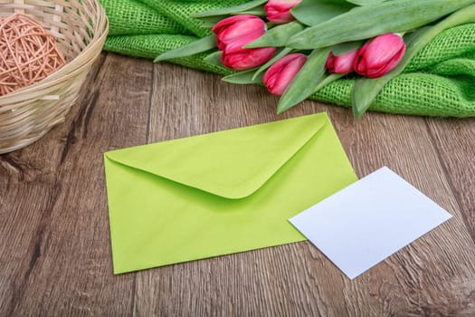 Envelope with sheet of paper and red tulips on a wooden background