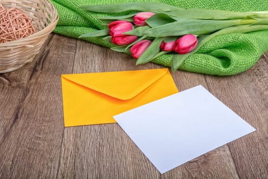 Envelope with sheet of paper and red tulips on a wooden background