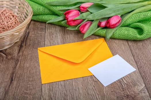 Envelope with sheet of paper and red tulips on a wooden background