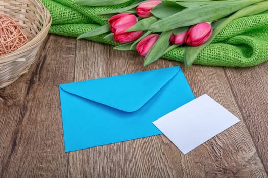 Envelope with sheet of paper and red tulips on a wooden background